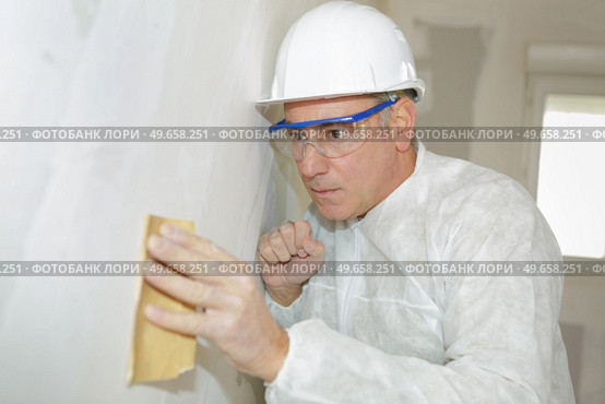 senior man wearing protection sanding interior wall for restoration. Стоковое фото, агентство Ingram Publishing / Фотобанк Лори