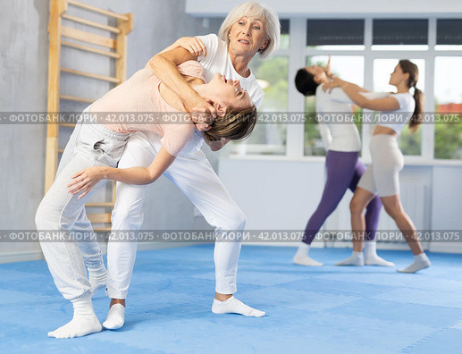 Senior woman applying inverted headlock during mock bout in self-defense training. Стоковое фото, фотограф Яков Филимонов / Фотобанк Лори