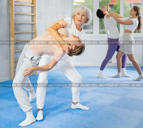 Senior woman applying inverted headlock during mock bout in self-defense training. Стоковое фото, фотограф Яков Филимонов / Фотобанк Лори