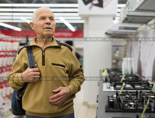 Senor man pensioner buying kitchen stove in showroom of electrical appliance store. Стоковое фото, фотограф Татьяна Яцевич / Фотобанк Лори