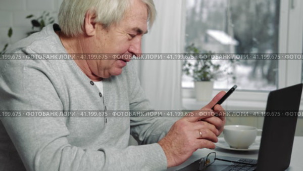 Serious senior man wearing glasses Talking mobile phone sitting at desk at home workplace with laptop. Retired male working chatting colleagues. Old worker talk on cellphone work on computer gadget. Стоковое видео, видеограф Марина Демидюк / Фотобанк Лори