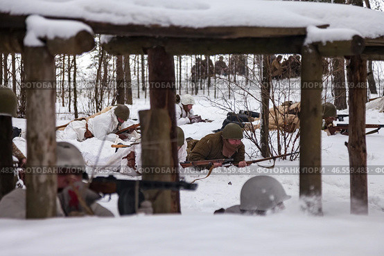 Sestroretsk, Russia - February 19, 2023: Soldiers reenact a WWII winter battle amidst snow-covered trees and makeshift cover at a historical restoration event. Редакционное фото, фотограф Aleksandr Golubev / Фотобанк Лори
