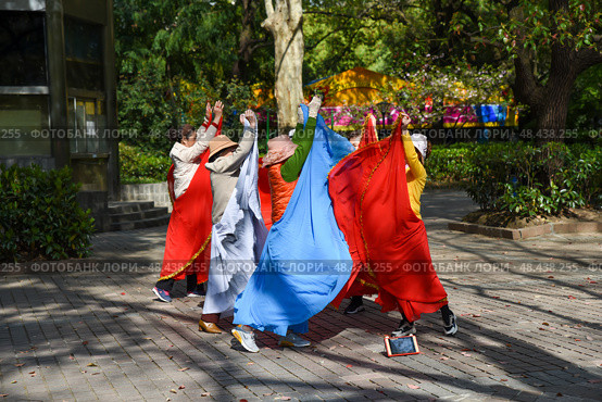 Shanghai, China - 1 April 2025: Senior Chinese women perform a colorful folk dance in People’s Park, gracefully moving in coordinated steps. Редакционное фото, фотограф Татьяна Терехина / Фотобанк Лори
