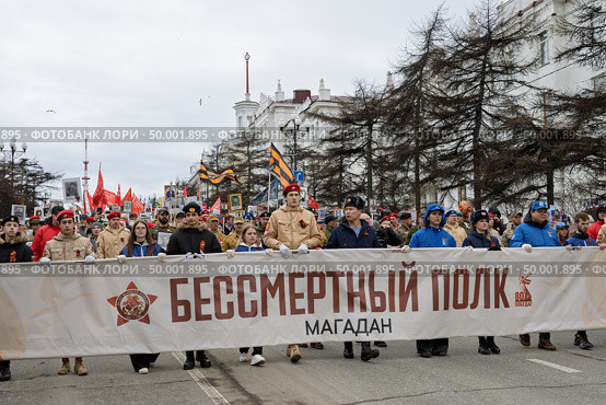 Шествие «Бессмертного полка» в Магадане, 9 мая 2025 года. День Победы. По проспекту Ленина идёт колонна демонстрантов с транспарантом «Бессмертный полк». Участники демонстрации несут красные флаги и портреты ветеранов войны. Празднование 80-летия победы Красной армии и советского народа над нацистской Германией в Великой Отечественной войне 1941–1945 годов. Город Магадан, Магаданская область, Россия. Редакционное фото, фотограф Андрей Степанов / Фотобанк Лори