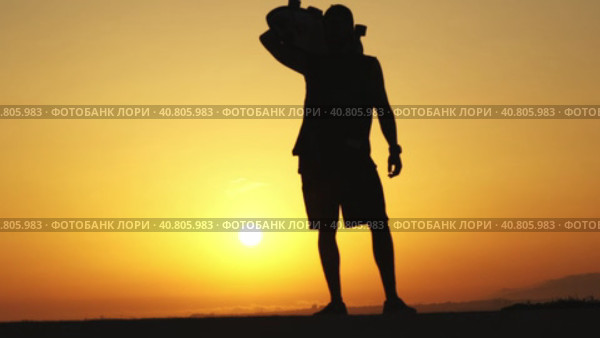 Silhouette of a man standing on sunset and with a longboard on his shoulder. Стоковое видео, видеограф Константин Шишкин / Фотобанк Лори