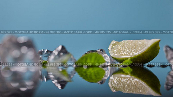 Slice of lime wedge, ice and mint isolated on blue background, ingredient for cold drink in summer. Slice of lime wedge, ice and mint isolated on blue background. Стоковое фото, агентство Ingram Publishing / Фотобанк Лори