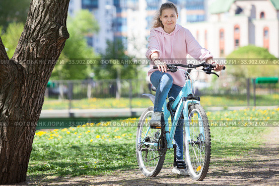 Smiling happy Caucasian teen age girl riding modern bicycle on a city park, looking at camera. Стоковое фото, фотограф Кекяляйнен Андрей / Фотобанк Лори