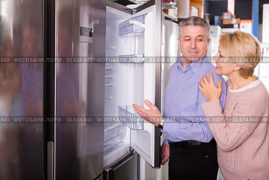 Smiling mature married couple choose for themselves refrigerator. Стоковое фото, фотограф Яков Филимонов / Фотобанк Лори