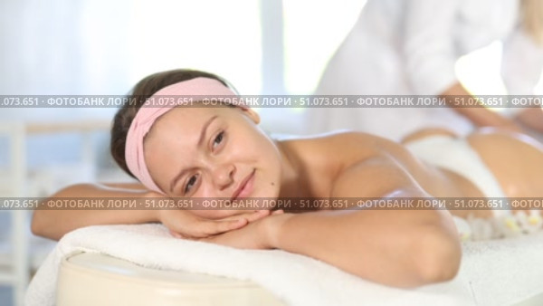 Smiling young woman relaxing on massage table in spa salon while skilled female therapist performing anti-cellulite thigh and butt massage. Стоковое видео, видеограф Яков Филимонов / Фотобанк Лори