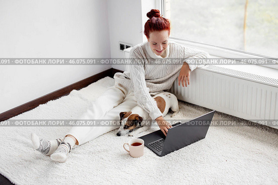 Smiling Young Woman Sitting on carpet and using Laptop by dog at Home. Стоковое фото, фотограф Гладских Татьяна / Фотобанк Лори