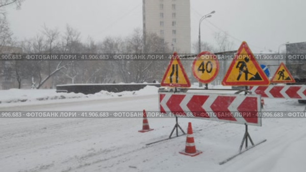 Снегопад в большом городе. Автомобили едут по заснеженной дороге. Дорожные знаки объезд, ремонтные работы, ограничение скорости. Сильный ветер и метель. Москва, Россия, 3 декабря 2023. Редакционное видео, видеограф Ирина / Фотобанк Лори