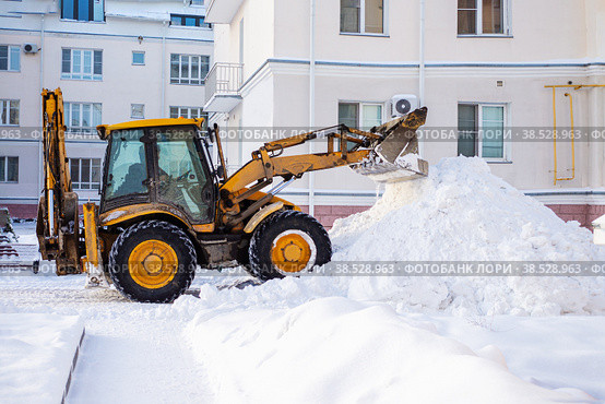 Snow removal equipment on the road in winter. Yellow excavator removes a huge mountain of snow. Clearing snow on the road in the city in a snowstorm. Стоковое фото, фотограф Оксана Медведева / Фотобанк Лори