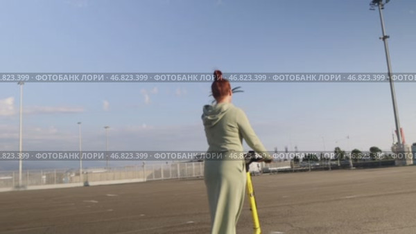 Sochi, Russia - 10 October, 2024: A red-haired beautiful woman rides a Yandex electric scooter in the Olympic Park. Стоковое видео, видеограф Арзюков Вадим Николаевич / Фотобанк Лори