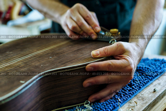 Soft focus of unrecognizable craftsman carving part for Spanish flamenco guitar on workbench during work in luthier workshop. Unrecognizable Spanish flamenco guitar luthier crafting guitar part. Стоковое фото, агентство Ingram Publishing / Фотобанк Лори