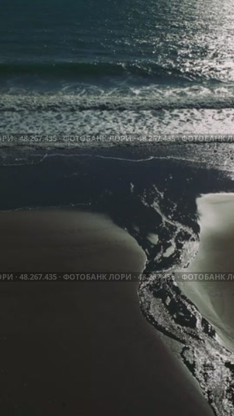 Soft sunset light illuminating dark sandy coastline, golden reflections rippling across wet shore with gentle waves washing over serene oceanfront landscape. Стоковое видео, видеограф ILIA GOROKHOV / Фотобанк Лори