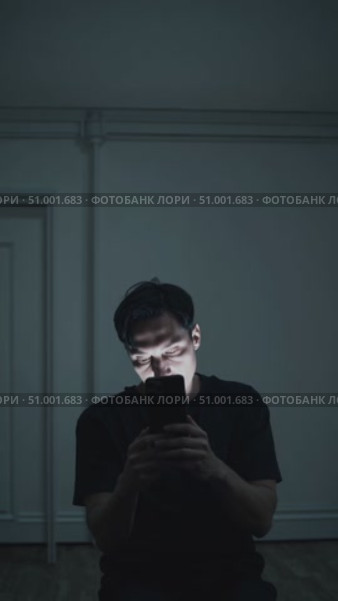 Solitary male silhouetted against dim interior, smartphone screen casting ghostly shadows while highlighting emotional isolation and digital disconnection. Стоковое AI-видео, аниматор Данил Руденко / Фотобанк Лори