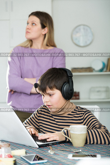 Son plaing video games at laptop, sad mom on background. Стоковое фото, фотограф Яков Филимонов / Фотобанк Лори
