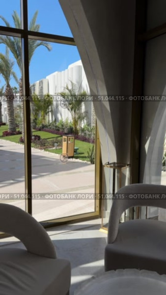 Современное здание с арочными элементами на фоне голубого неба The villa is a modern, white Mediterranean-style house with arched doorways, large balconies, and light stone elements, surrounded by a landscaped rocky garden and a clear blue sky. Стоковое видео, видеограф Zita Khasanova / Фотобанк Лори