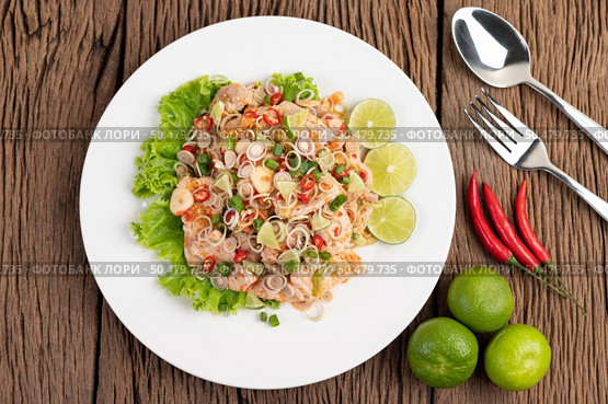Spicy pork salad with galangal, lemon, chilli, garlic and put in a salad on a white plate, On wooden Table. Стоковое фото, агентство Ingram Publishing / Фотобанк Лори
