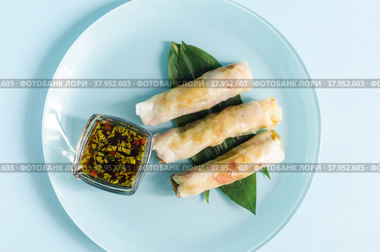 Спринг-роллы из морепродуктов и овощей с декором из зеленых листьев на светлом фоне. Стоковое фото, фотограф Лозовая Людмила / Фотобанк Лори