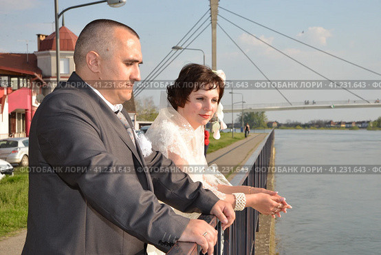 Sremska Mitrovica, Serbia October 10, 2019 a groom in a gray suit and a bride in a white dress are standing by the river. Стоковое фото, фотограф Юлия Петровская / Фотобанк Лори