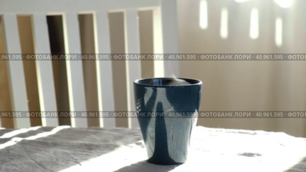 Steaming Cup of Coffee or Tea on Table. White linen Tablecloth. Close-up ceramic blue mug with smoke on old table in dining room interior background. Hot Drink Concept. Cozy Morning. Стоковое видео, видеограф Марина Демидюк / Фотобанк Лори