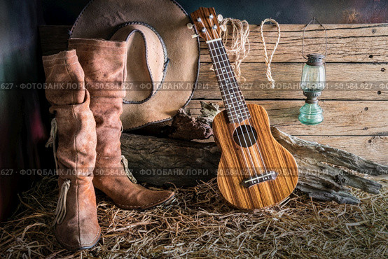 Still life painting photography with ukulele on american west rodeo brown felt cowboy hat and traditional leather boots in vintage ranch barn background. Стоковое фото, агентство Ingram Publishing / Фотобанк Лори