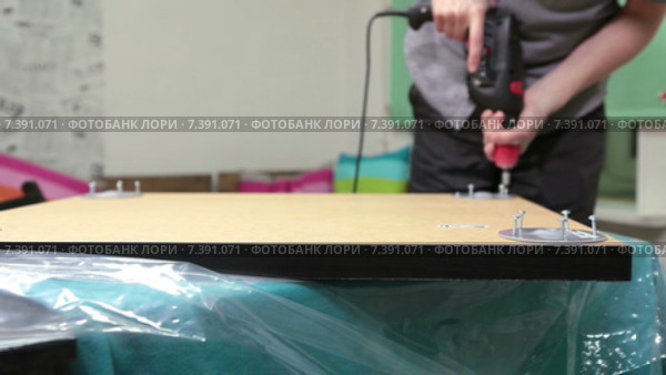 Столяр вкручивает саморезы шуруповертом для крепления ножек стола. Стоковое видео, видеограф Кекяляйнен Андрей / Фотобанк Лори