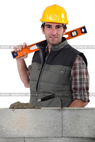Stonemason standing before a wall and carrying a spirit level. Стоковое фото, агентство Ingram Publishing / Фотобанк Лори