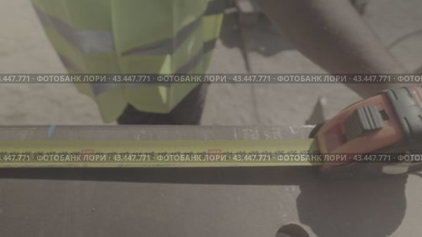 Строитель в жилетке измеряет рулеткой железную конструкцию a builder in a vest measures an iron structure with a tape measure. Стоковое видео, видеограф Опока Алексей / Фотобанк Лори