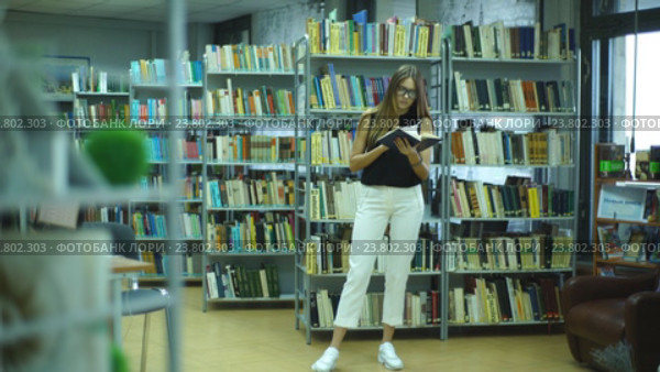 Студентка пролистывает книгу, стоя в библиотеке. Стоковое видео, видеограф Виктор Аллин / Фотобанк Лори