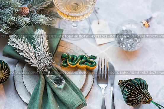 Stylish plates, napkin, glass, champagne, Christmas tree branches and Christmas decorations on a gray background. Table setting. The concept of Merry Christmas and New Year 2025. Стоковое фото, фотограф Photojuli / Фотобанк Лори