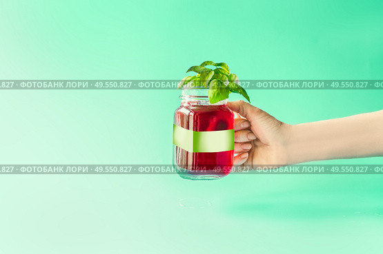 Summer drink in female hand. Red refreshing berries beverage in glass jar with green white branding mock up at sunny bight mint background. Summer mood. Blank Label at juice bottle. Стоковое фото, агентство Ingram Publishing / Фотобанк Лори