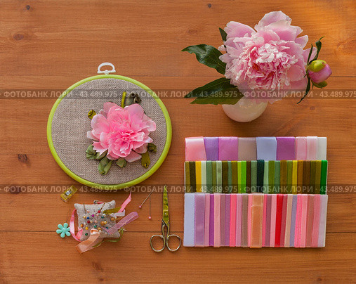 Summer floral hand embroidery with satin ribbons of peony flowers in hoop, bouquet of fresh peonies on wooden table. Nearby is set of colorful satin ribbons, needles and scissors for work. Flat lay, close-up. Стоковое фото, фотограф Виктория Катьянова / Фотобанк Лори