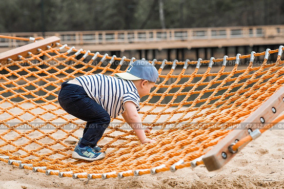 Summer lifestyle. A cute little boy is having fun playing in a hammock on the beach on a modern playground. The concept of family entertainment and leisure. Стоковое фото, фотограф Photojuli / Фотобанк Лори