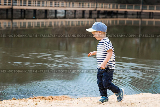 Summer lifestyle. A cute little boy is having fun playing with sand on the beach by the water. The concept of family entertainment and leisure. Стоковое фото, фотограф Photojuli / Фотобанк Лори