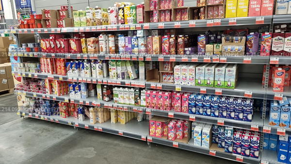 Supermarket shelf with a large selection of drinks and dairy products in tetra pack cardboard packaging. The shelves feature different brands and types of products: milkshakes, yoghurts, cream, milk, as well as plant-based alternatives — soy, oat, almond milk. The packaging is brightly colored: pink, yellow, white, blue, and green, creating a rich palette. Popular brands such as Domik v Derevne, Selo Zelenoe, Valio, Bite, Nemoloko, and others are visible. The bottom row also features yoghurts and desserts in plastic cups. The atmosphere of the photo emphasizes the variety of products and the modern retail format. Редакционное фото, фотограф Анна Кривицкая / Фотобанк Лори
