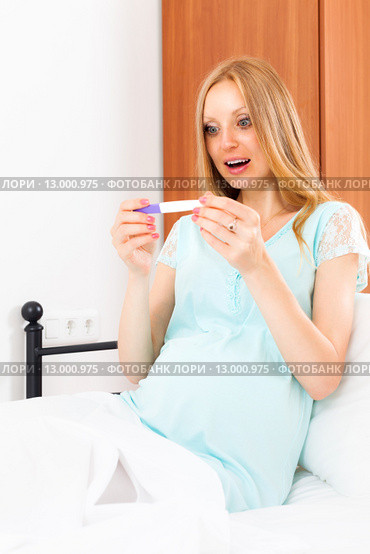 Suprised pregnant woman with pregnancy test at home interior. Стоковое фото, фотограф Яков Филимонов / Фотобанк Лори