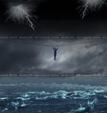 Surviving the storm business concept with a businessman hanging on to a tightrope crossing over dangerous water as a concept and metaphor for conquering adversity and overcoming challenges. Стоковое фото, агентство Ingram Publishing / Фотобанк Лори