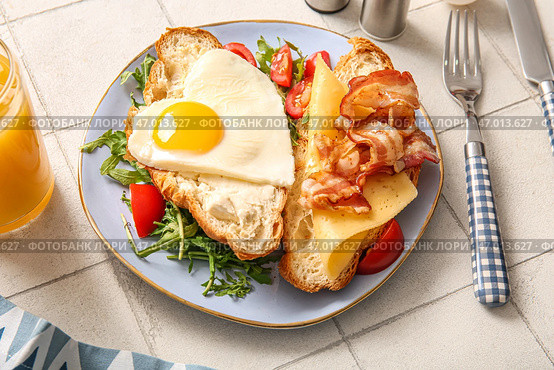 Тарелка с вкусным жареным яйцом, нарезанным круассаном, беконом, помидорами и стакан сокa на светлом фоне плитки, крупным планом. Стоковое фото, фотограф Pixel_shot / Фотобанк Лори