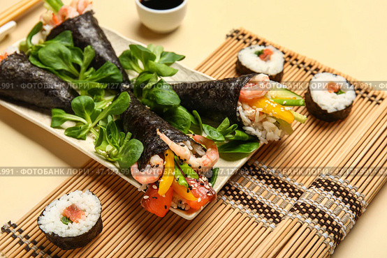 Тарелка с вкусными конусами суши, роллами, листовым салатом и бамбуковым ковриком на цветном фоне, крупным планом. Стоковое фото, фотограф Pixel_shot / Фотобанк Лори