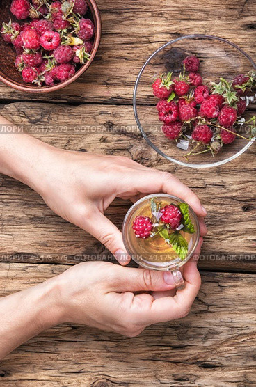 Tea with raspberries. Tea cup with raspberry warming tea in hands on vintage wooden background. Стоковое фото, агентство Ingram Publishing / Фотобанк Лори