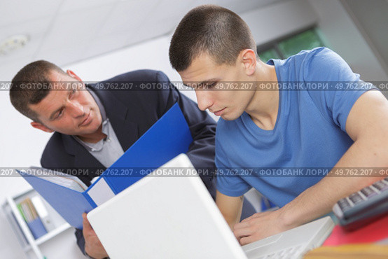 Teacher helping young man using laptop. Стоковое фото, агентство Ingram Publishing / Фотобанк Лори