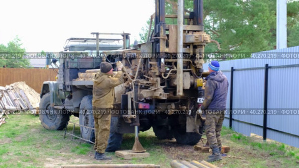 Team of workers with drilling rig on car are drilling artesian well for water in ground. Insertion of metal casing pipe into ground, installation of individual drinking supply, June 28, 2022, Russia, Palaces. Редакционное видео, видеограф Ольга Симонова / Фотобанк Лори
