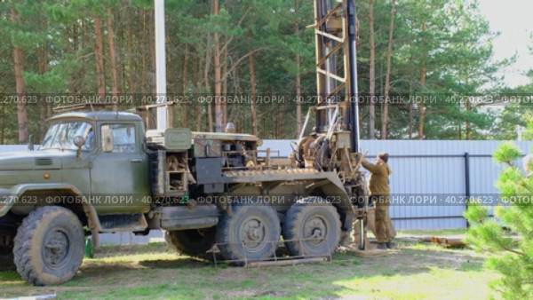 Team of workers with drilling rig on car are drilling artesian well for water in ground. Insertion of metal casing pipe into ground, installation of individual drinking supply, June 28, 2022, Russia, Palaces. Редакционное видео, видеограф Ольга Симонова / Фотобанк Лори