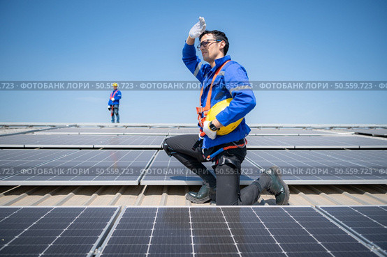 Technician repairing solar panels take off his hat and rest in the scorching sun on a factory roof covered with solar panels to receive solar energy. Стоковое фото, агентство Ingram Publishing / Фотобанк Лори
