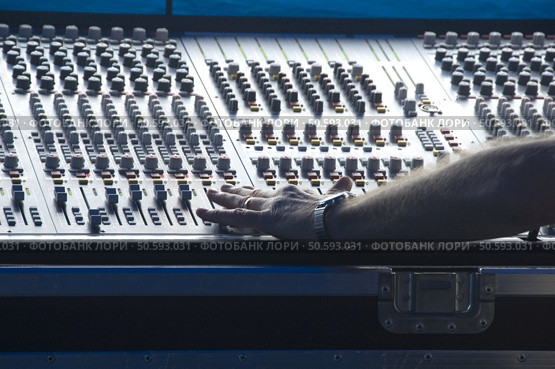 Technician's left hand makes adjustment on audio control panel in booth at outdoor concert. Стоковое фото, агентство Ingram Publishing / Фотобанк Лори