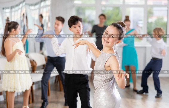 Teen girl in elegant evening dress dances incendiary twist with boy partner during choreography lesson. Стоковое фото, фотограф Яков Филимонов / Фотобанк Лори