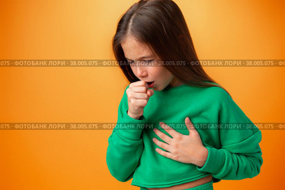 Teen girl wearing casual clothes feeling unwell and coughing against orange background. Стоковое фото, фотограф Сергей Толмачёв / Фотобанк Лори
