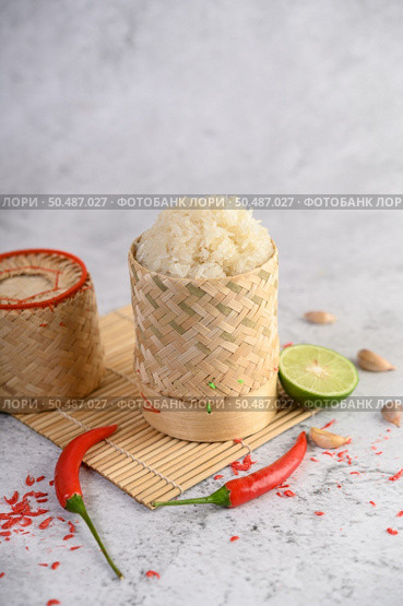 Thai sticky rice in a woven bamboo basket on a wooden panel with chilies, lime, and garlic. Selective focus. Стоковое фото, агентство Ingram Publishing / Фотобанк Лори